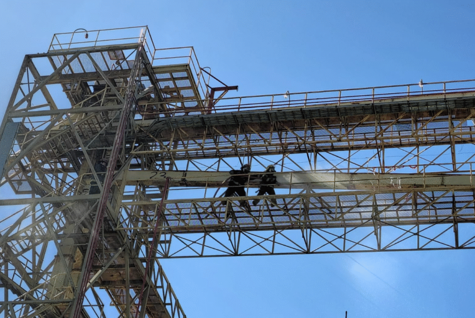 Dos trabajadores realizan tareas de mantenimiento en una estructura metálica elevada bajo un cielo despejado.